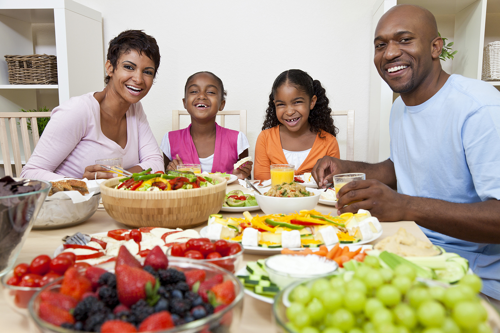 An attractive happy African American, smiling family of mother, father, two daughters eating salad and healthy food at a dining table.